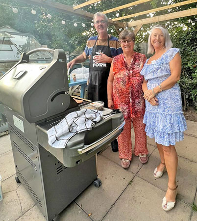 A man and two women pose by a barbecue